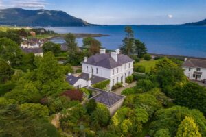 Exterior of 12 Rostrevor Road, a mansion for sale in Co. Down. Carlingford Lough can be seen to the right side of the property. Gardens shrubs and trees surround the house.