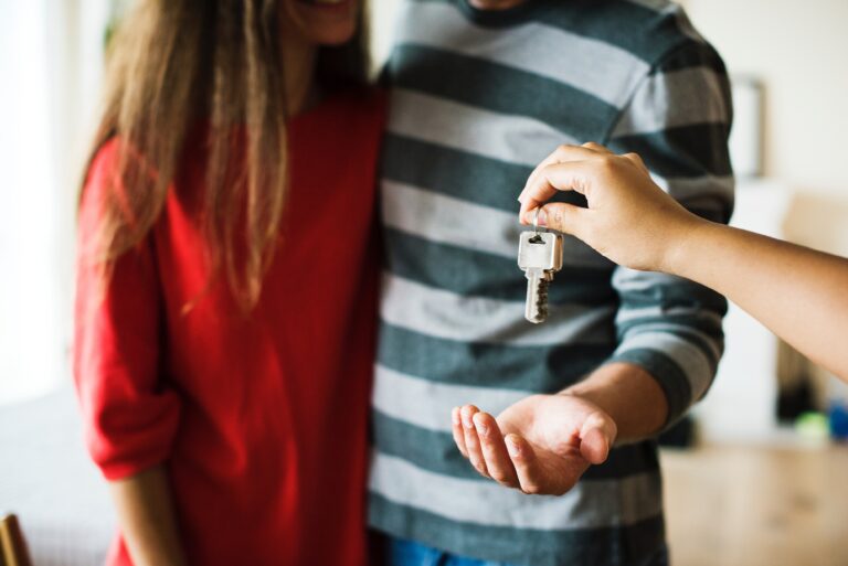 Young couple moving home. Someone is handing the couple the key to their new home.