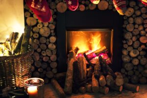 Featured image for the prepare your house for winter blog. This image focuses on a lit fireplace with wooden logs surrounding the fireplace.