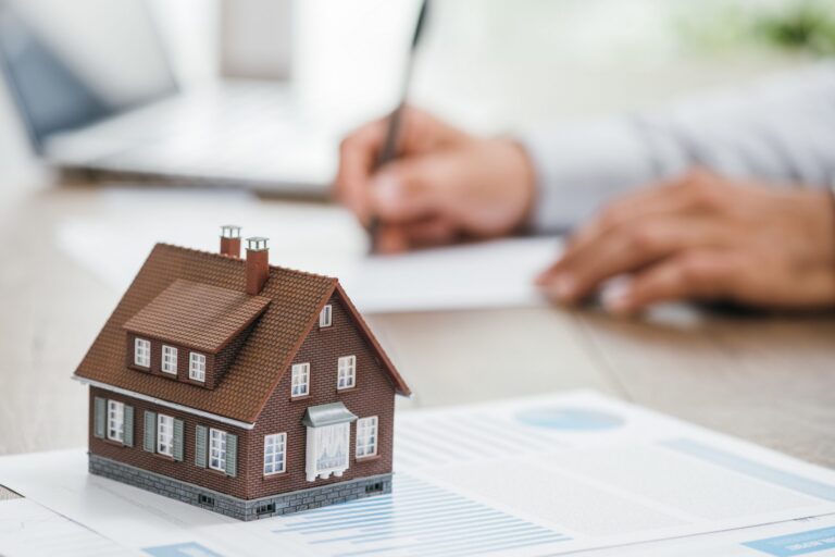 Estate Agent working in the background on the image while a model of a house sits on top of his paper work. Image used in the the guide to understanding mortgages article