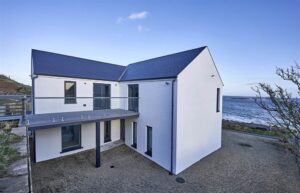 The exterior of 25 Rocks Road. This is a house for sale in Ballyhornan. The Irish Sea can be seen in the background. A balcony is seen to the front of the image.