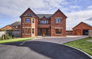 The exterior of 11 Ballycrochan Park, a large detached home in Bangor. A brick driveway leads to the detached, double garage which is found to the right of the property. Neat lawns are found to either side of the driveway.