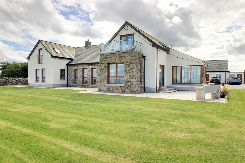 The exterior of 4 Stoneyfalls Lane. This is a detached property for sale in Ballyhalbert. Well-maintained lawns can be found to the front of the property. There is also a paved area with a stone seat.